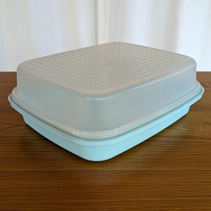 以下が含まれることがあります： 長方形の食品保存容器。明るい青色のベースと、それに合わせた、わずかに半透明の蓋が付いています。蓋には、格子状のテクスチャパターンがあります。この容器は、食品の保存と整理のために設計されています。