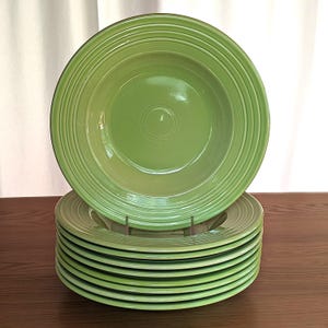 May include: A stack of green ceramic plates with a ridged design. One plate is on top of the stack, and the plates are displayed on a brown metal plate stand. The plates are a bright, solid green color.