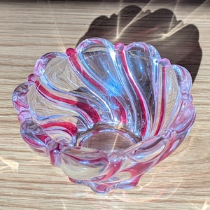 May include: A clear glass bowl with a swirl design in pink. The bowl is perfect for holding small items like jewelry or candy.