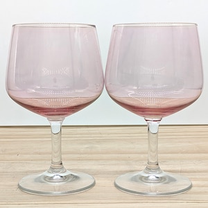 May include: Two pink-tinted wine glasses. The glasses have a rounded bowl and a clear, slender stem. The base of the bowl and the stem are a darker shade of pink. The glasses are made of clear glass. The glasses are suitable for wine.