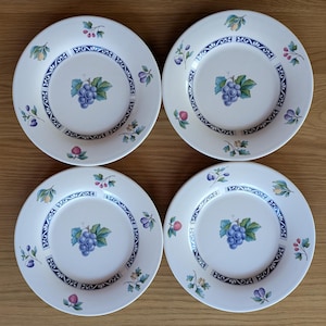 May include: Set of four white ceramic dinner plates with a blue and green floral design. Each plate features a grape cluster and leaves in the center, surrounded by a decorative border.