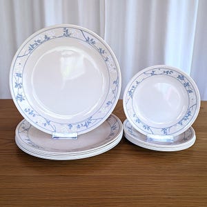 Puede incluir: Un juego de platos de cerámica blanca con un diseño floral en azul y blanco. Los platos están apilados, con tamaños más grandes y más pequeños. El patrón floral rodea los bordes de los platos.