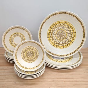 May include: A set of vintage cream-coloured dinnerware with a yellow and brown floral pattern. The collection includes plates and bowls of different sizes, ideal for a retro kitchen. The plates and bowls are made of ceramic.