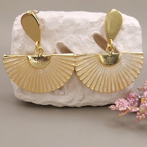 Puede incluir: Pendientes dorados con diseño en forma de abanico. Los pendientes presentan una pieza superior en forma de lágrima conectada a un diseño de abanico semicircular con líneas radiales. La parte del abanico es de color blanco crema con ribete dorado.