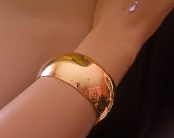 Könnte beinhalten: Ein goldfarbenes Armreif-Armband mit einer glatten, abgerundeten Oberfläche.
