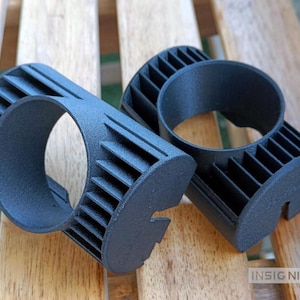 Könnte beinhalten: Zwei mattschwarze 3D-gedruckte Komponenten mit einer zylindrischen Mittelöffnung, die von einer Reihe vertikaler Kühlrippen umgeben ist. Jedes Teil hat eine gekerbte Basis und der Text INSIGNIAS3D ist unten rechts im Bild zu sehen.