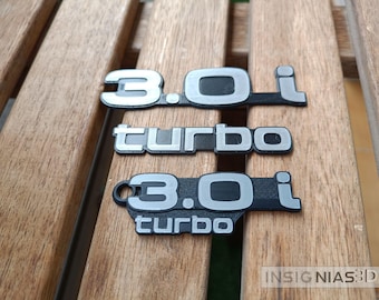 Może przedstawiać: Trzy czarne i srebrne emblematy samochodowe. Górny emblemat zawiera napis "3.0i". Środkowy emblemat zawiera napis "turbo". Dolny emblemat zawiera napis "3.0i turbo".