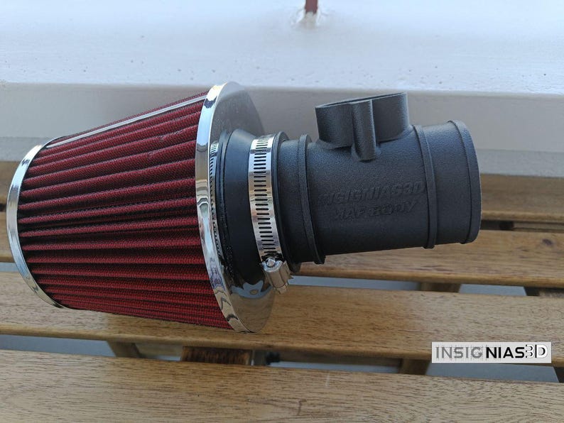Może przedstawiać: Stożkowy filtr powietrza z ciemnoczerwonego plisowanego materiału z polerowaną chromowaną nasadką, przymocowany do matowego czarnego cylindrycznego adaptera wlotowego. Adapter posiada metalową opaskę zaciskową oraz wytłoczony napis INSIGNIAS3D MAF BODY.