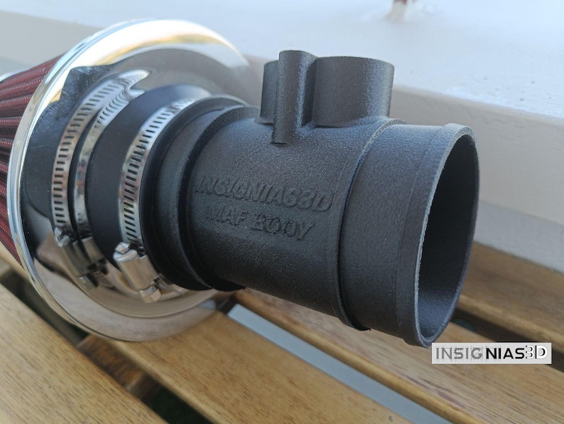 Może przedstawiać: Czarny matowy adapter korpusu MAF z wytłoczonym napisem INSIGNIAS3D MAF BODY, połączony z cylindrycznym czerwonym filtrem powietrza z chromowaną metalową krawędzią za pomocą dw&oacute;ch srebrnych metalowych opasek zaciskowych. Element ma teksturowane wykończenie.