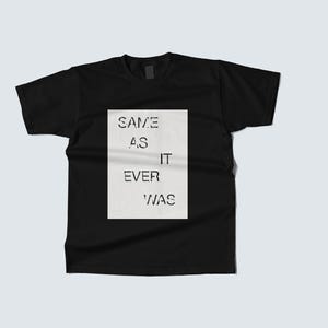 May include: Black t-shirt with a rectangular white graphic on the front. The graphic features the text "SAME AS IT EVER WAS" in a sans-serif font. The shirt is displayed on a light grey background.
