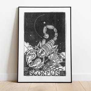 May include: Black and white framed art print featuring a detailed illustration of a scorpion with a curved tail under a crescent moon and stars. The word "SCORPIUS" is at the bottom of the print. The artwork is displayed on a wooden floor.