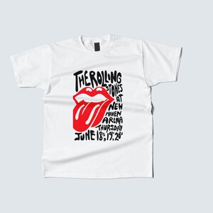 May include: White t-shirt featuring a red and black graphic. The graphic includes the words "THE ROLLING STONES" above a red tongue logo, with additional text indicating a concert at New Haven Arena on June 18, 1979. A classic rock and roll tee.