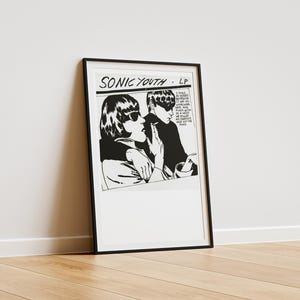 Puede incluir: Impresi&oacute;n enmarcada en blanco y negro con una ilustraci&oacute;n de estilo pop art de dos personas con gafas de sol. La impresi&oacute;n tiene el texto "SONIC YOUTH - LP" en la parte superior. La imagen est&aacute; apoyada contra una pared blanca sobre un suelo de madera.