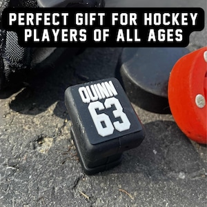 Custom hockey stick end cap topper personalized with player name and number, displayed with hockey equipment, gift idea for players.