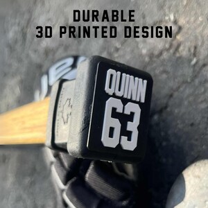 Durable 3D printed hockey stick end cap topper featuring custom name and number design, securely fitted on stick.