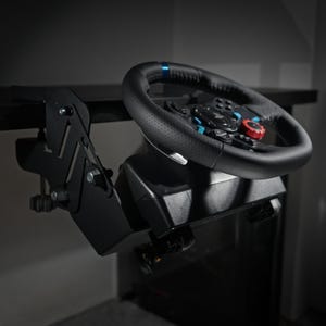 Puede incluir: Un volante de juego negro con detalles azules y rojos, montado en un soporte negro. El volante está fijado a una base negra, diseñado para su uso con un ordenador. El volante es de cuero negro y tiene varios botones.