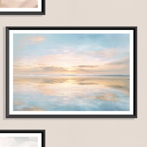 Può includere: Stampa incorniciata di una serena scena di spiaggia al tramonto. Il cielo passa dall'azzurro chiaro al pesca e all'oro, riflettendosi nell'acqua calma. L'opera d'arte è racchiusa in una cornice nera, creando un'estetica minimalista.