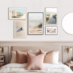 May include: A collection of framed beach-themed art prints. The prints feature coastal scenes, including beach huts, a sandy beach with a shell, a wooden walkway to the sea, and seashells. The frames are in gold and black, creating a cohesive gallery wall.