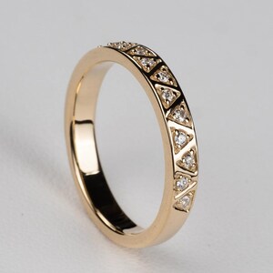 May include: A gold ring with a repeating pattern of small triangles, each containing a small, clear stone. The ring has a smooth, polished band and a bright, reflective surface. The ring is a piece of jewelry.