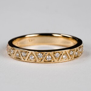 May include: A gold band ring with a repeating pattern of triangles, each containing a small, clear gemstone. The ring has a polished finish and is set against a white background. The ring is a delicate piece of jewelry.