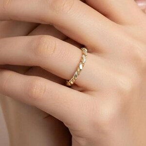 May include: A gold ring with a textured, braided design. The ring is worn on a finger, showcasing its intricate pattern and warm, metallic color. The ring's design is a continuous loop, creating a classic and elegant look.