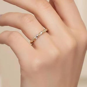 May include: A gold-colored ring with a textured design, featuring small, raised details. The ring is worn on a finger, showcasing its intricate pattern and subtle shine. The jewelry piece is a delicate accessory.