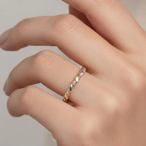May include: A gold-colored ring with a twisted rope design. The ring is worn on a finger, showcasing its intricate texture and shine. The ring's design is a continuous pattern, reflecting light and adding a touch of elegance.