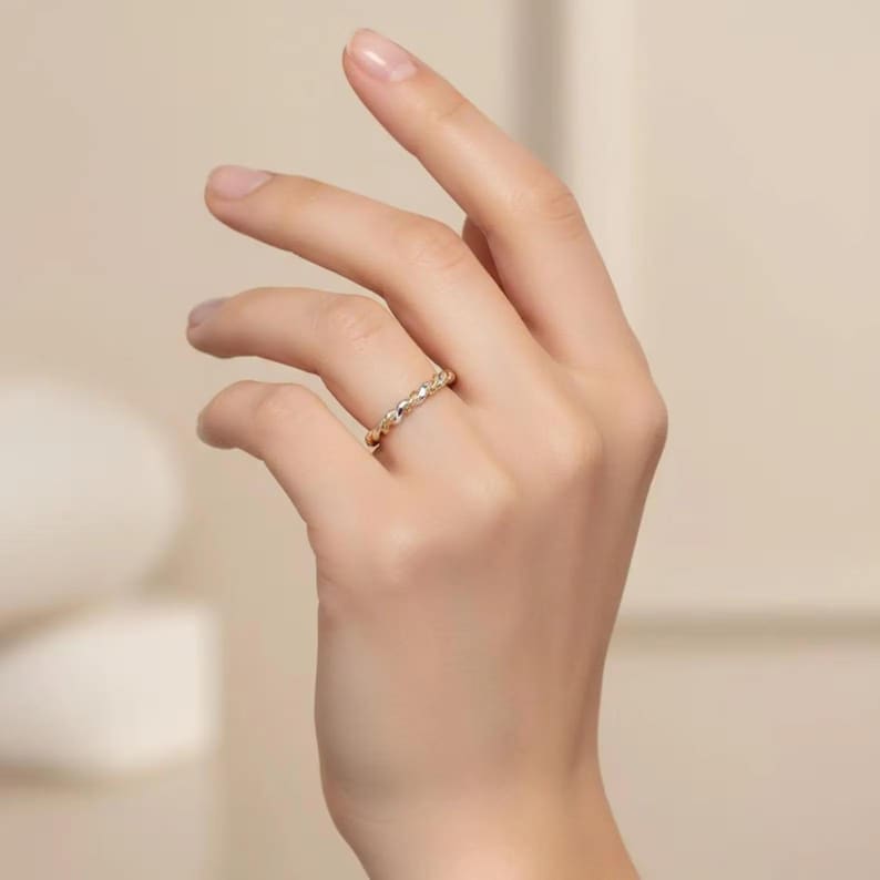 May include: A gold-colored ring with a textured design, featuring small, raised details. The ring is worn on a finger, showcasing its intricate pattern and subtle shine. The jewelry piece is a delicate accessory.