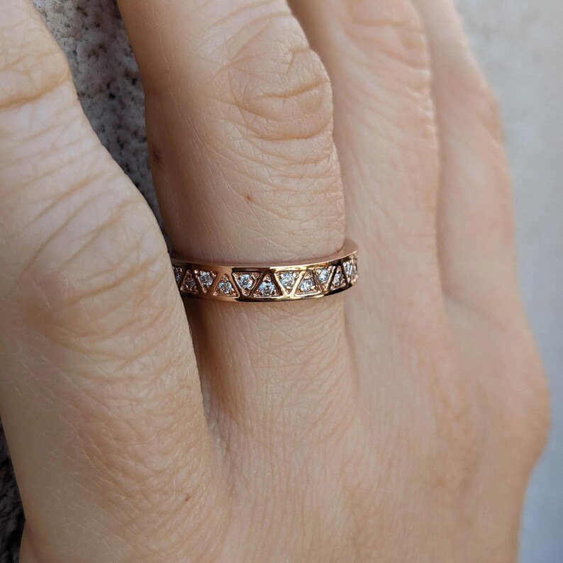 May include: Rose gold ring with a geometric design. The ring features a series of triangles, each set with a small, clear gemstone. The band is a warm, metallic color, and the gemstones sparkle.