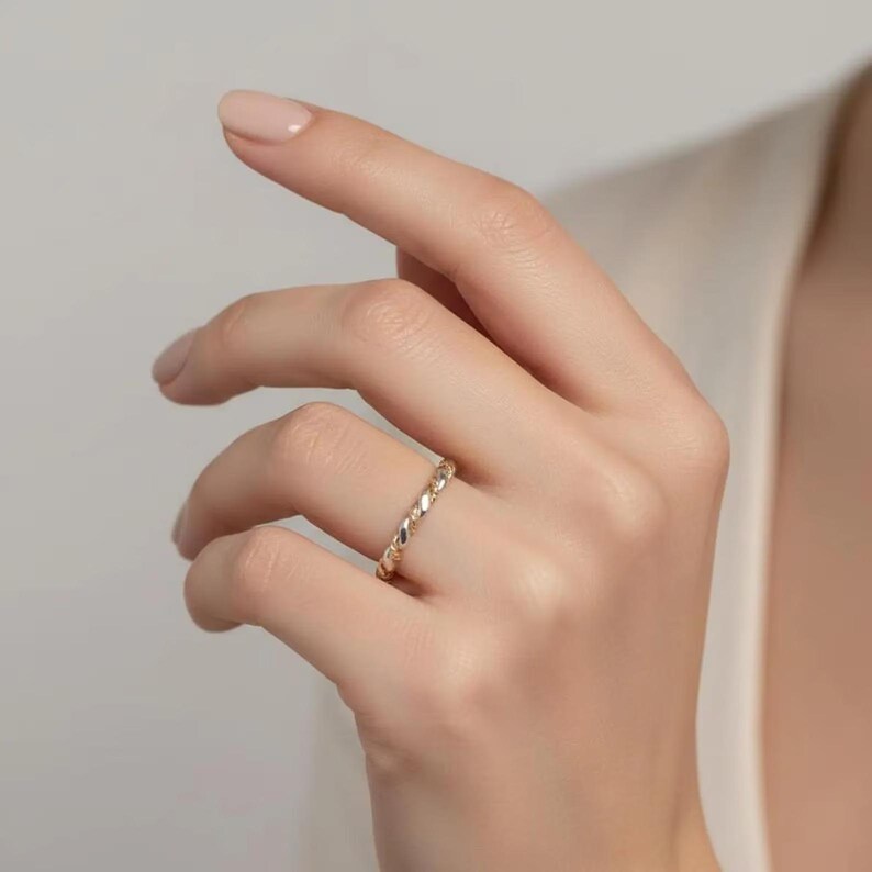May include: A gold-colored ring with a twisted rope design. The ring is worn on a finger, showcasing its intricate texture and shine. The ring's design is a continuous pattern, reflecting light and adding a touch of elegance.