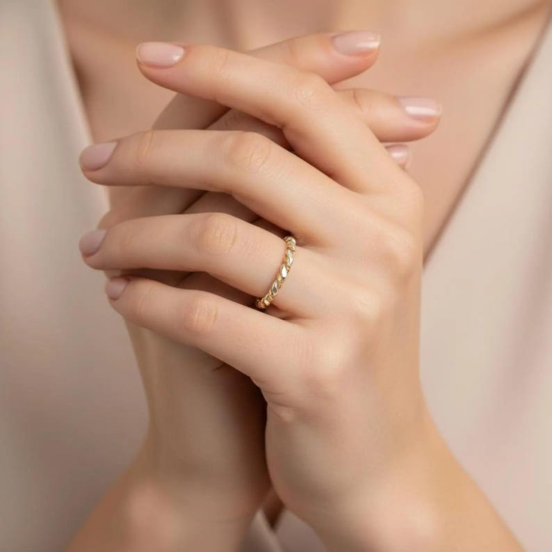 May include: A gold ring with a textured, braided design. The ring is worn on a finger, showcasing its intricate pattern and warm, metallic color. The ring's design is a continuous loop, creating a classic and elegant look.
