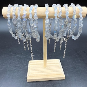 May include: A collection of bracelets made from irregular, translucent moonstone chips with iridescent blue flashes. Each bracelet features a silver-toned metal lobster clasp and an adjustable extender chain with a small teardrop-shaped charm at the end.