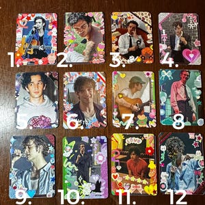 May include: Twelve colorful cards with a white border, each featuring a different photo of a person. The cards are decorated with colorful stickers and glitter.