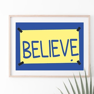 Puede incluir: Una impresi&oacute;n enmarcada con fondo amarillo y borde azul. La palabra "BELIEVE" est&aacute; escrita en azul sobre el fondo amarillo.