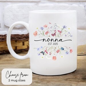 May include: White ceramic mug with a floral design in shades of pink, blue, and green. The mug has the word "nonna" written in black cursive script with the text "EST. 2025" below it.