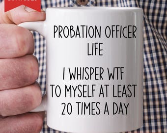 Puede incluir: Taza de cerámica blanca con el texto "PROBATION OFFICER LIFE I WHISPER WTF TO MYSELF AT LEAST 20 TIMES A DAY". La taza tiene un asa blanca y el texto es negro. La taza está sujeta por una persona.