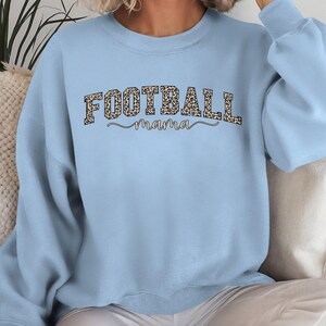 May include: A light blue sweatshirt with the words "FOOTBALL mama" printed across the front. The word "FOOTBALL" is in a leopard print pattern, and "mama" is in a cursive font.