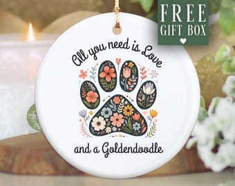 May include: White ceramic ornament with a floral paw print design. The ornament has the text "All you need is Love and a Goldendoodle." A gold string is attached for hanging. The words "FREE GIFT BOX" are in a green box.