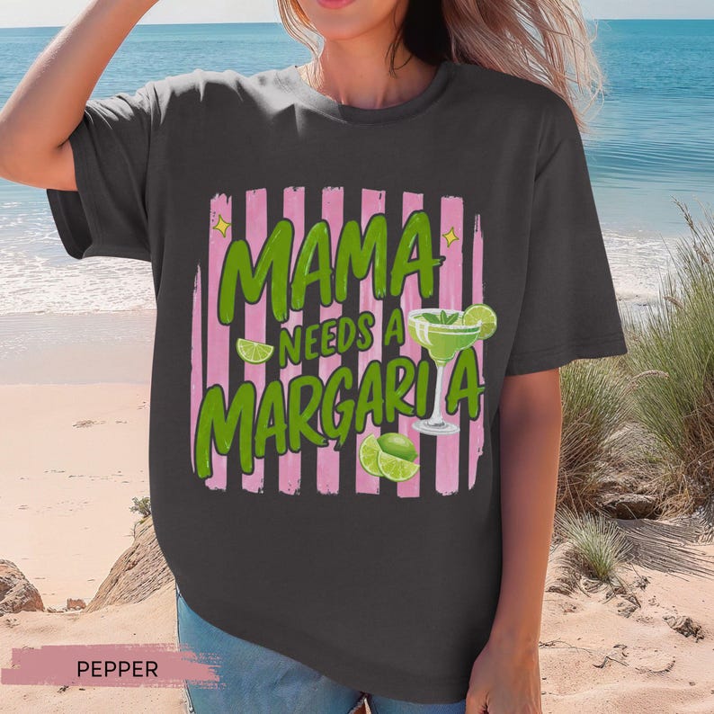 May include: A dark gray t-shirt with the text "MAMA NEEDS A MARGARITA" in green, with a margarita glass graphic and pink vertical stripes. The shirt also features lime slices.