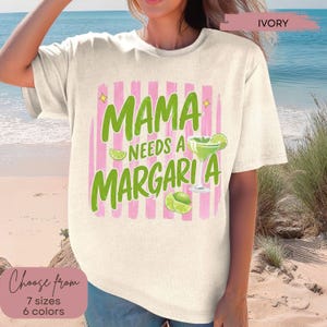 May include: Ivory-colored t-shirt with the text "MAMA NEEDS A MARGARITA" in green, accented with pink stripes and margarita illustrations. The shirt is available in 7 sizes and 6 colors.