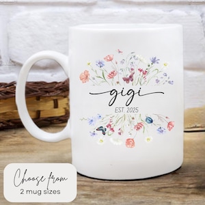 May include: White ceramic mug with a floral design and the text "gigi est. 2025". The flowers are in shades of pink, blue, and green. The mug has a black handle.