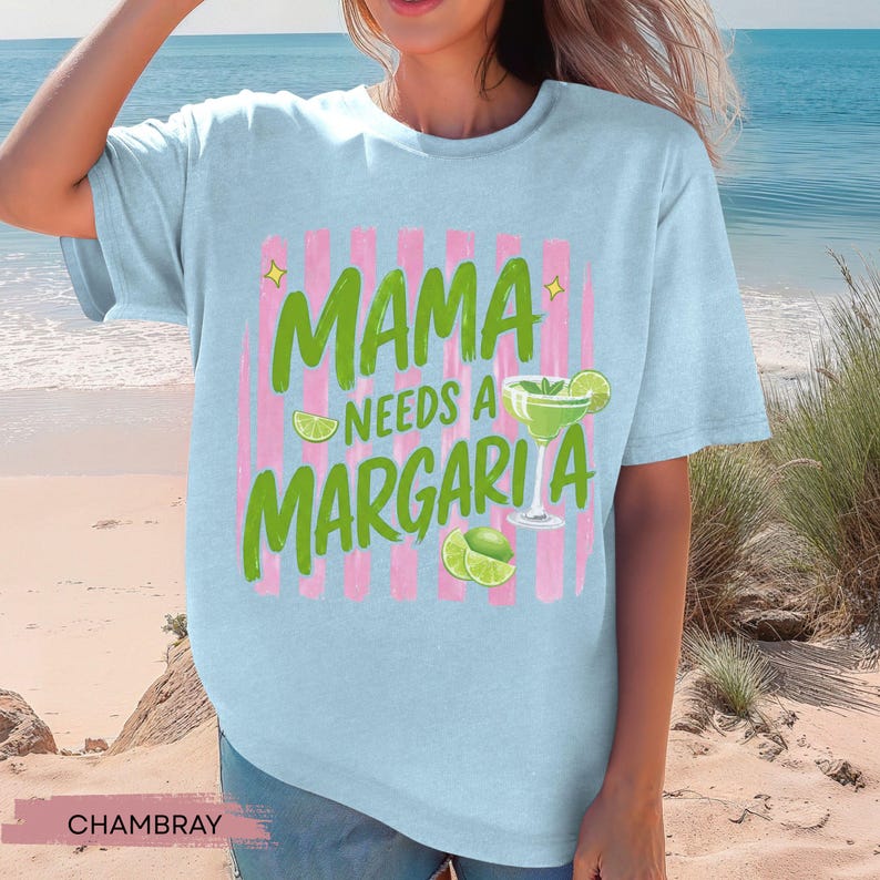 May include: Light blue t-shirt with the text "MAMA NEEDS A MARGARITA" in green, with a margarita glass and lime slices. The text is set against pink vertical stripes. The shirt is made of chambray fabric.