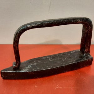 May include: A vintage cast iron flat iron with a handle. The iron is black and has a rustic appearance.