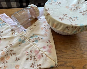 May include: A set of three reusable food wraps made of fabric with a floral pattern in shades of pink, blue, and brown. The wraps are shown on a wooden surface.