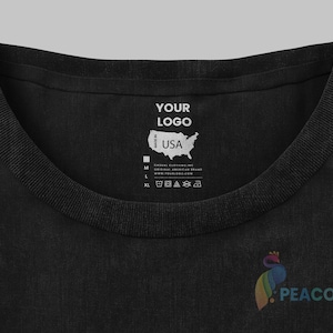 May include: Black t-shirt with a white label that says "YOUR LOGO" and "Made in USA". The label also includes a map of the United States and size information. The t-shirt has a peacock logo on the bottom right.