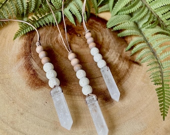 May include: Three crystal point necklaces with brown and white beads. The necklaces are hanging on a wooden surface.