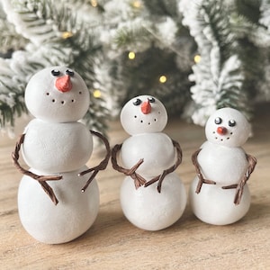 Könnte beinhalten: Drei weiße Schneemann-Ornamente mit braunen Zweig-Armen. Der Schneemann links ist der größte und hat drei Kugeln. Der mittlere Schneemann hat zwei Kugeln und der Schneemann rechts ist der kleinste mit einer Kugel.