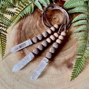May include: Three clear quartz crystal points are attached to a brown leather cord with brown wooden beads and brown lava rock beads.