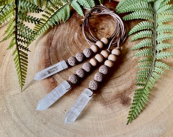 May include: Three clear quartz crystal points are attached to a brown leather cord with brown wooden beads and brown lava rock beads.
