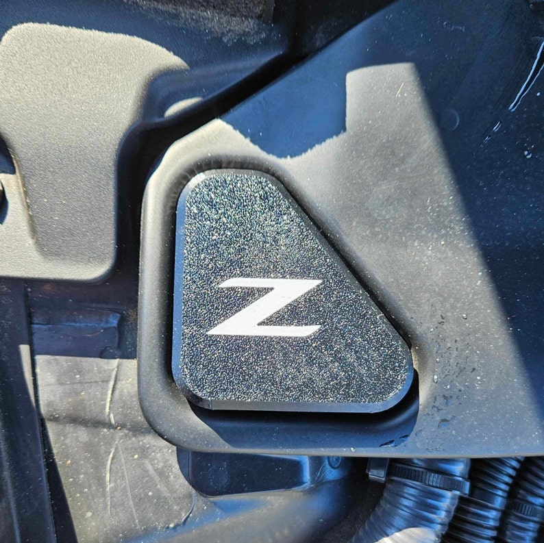 May include: A close-up of a black engine compartment with a textured black triangular panel featuring a white "Z" logo.